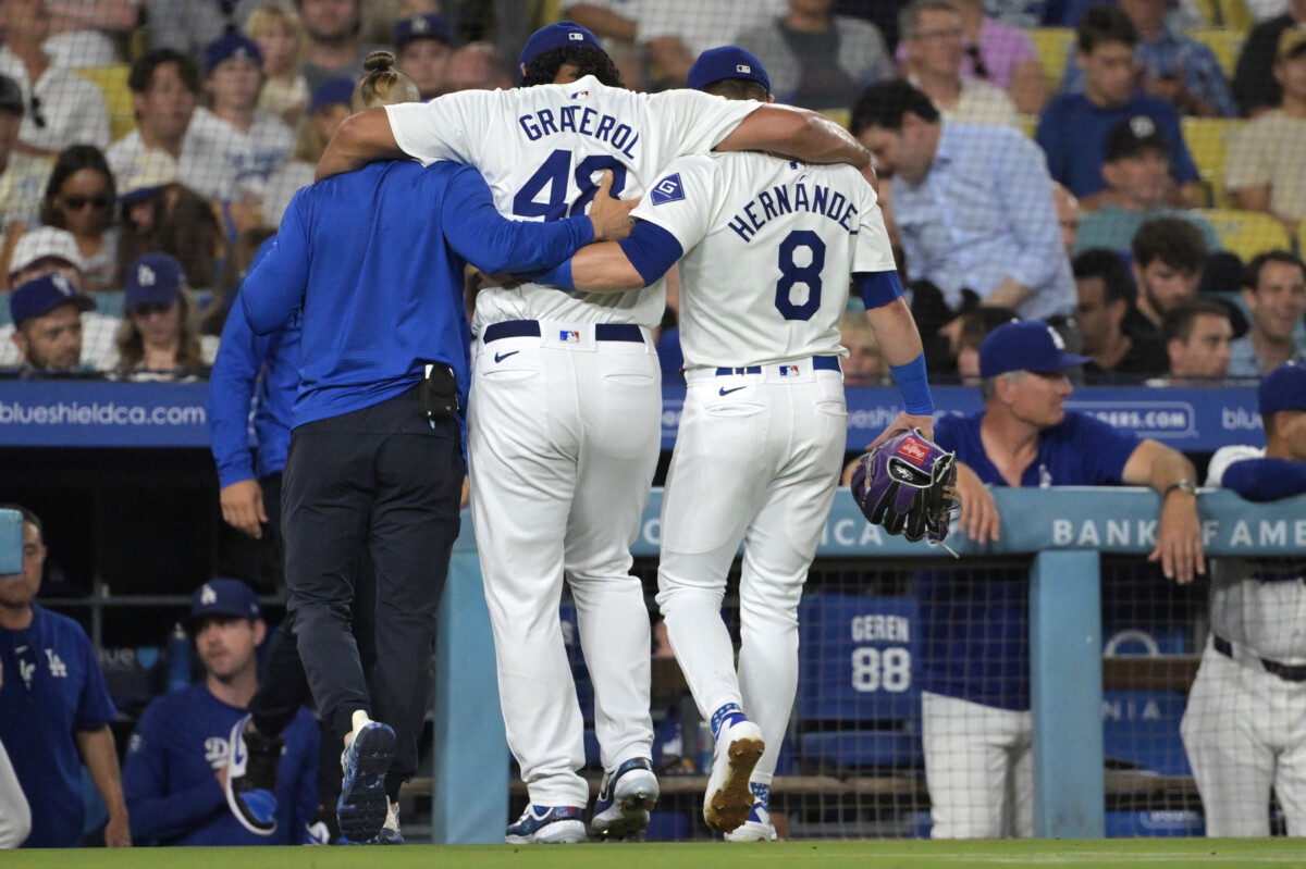 Aug 6, 2024; Los Angeles, California, USA;  Los Angeles Dodgers relief pitcher Brusdar Graterol (41) is helped off the field by trainer Thomas Albert and third baseman Enrique Hernandez (8) in the sixth inning after a hamstring injury against the Philadelphia Phillies at Dodger Stadium. Mandatory Credit: Jayne Kamin-Oncea-USA TODAY Sports