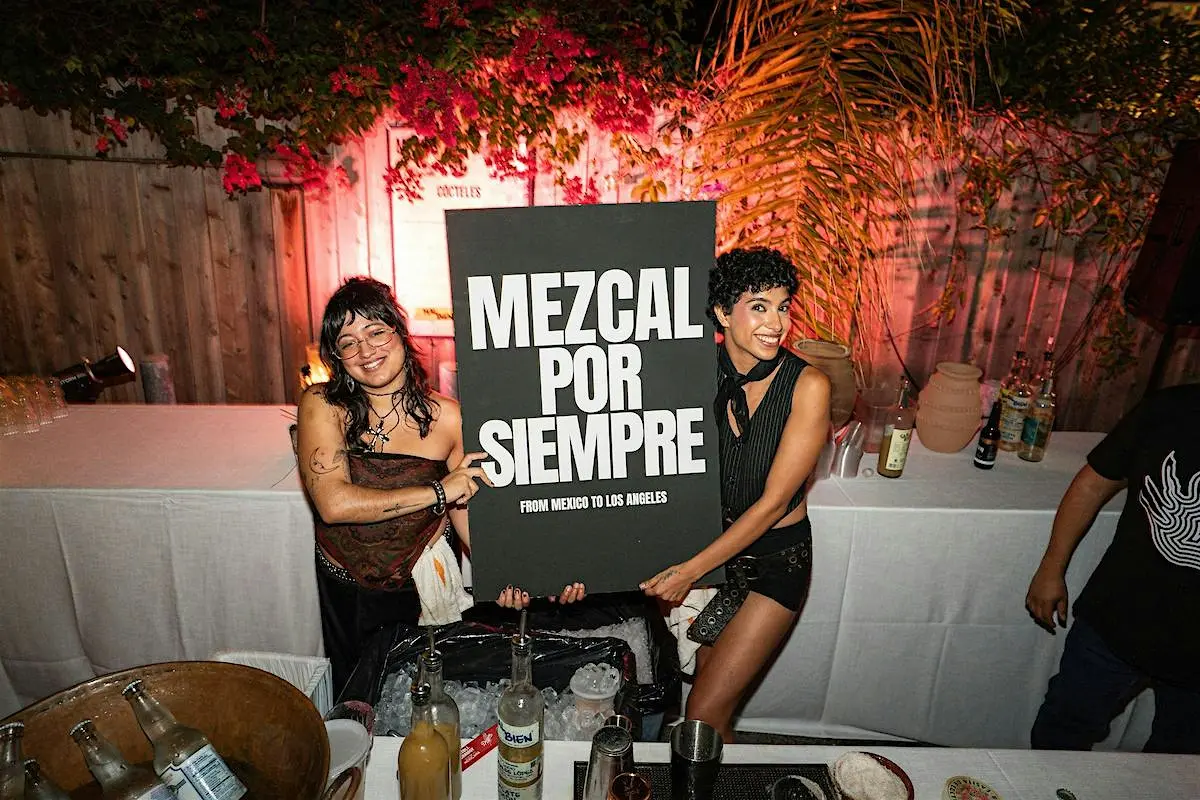 Women hold a sign commemorating the Mezcal Por Siempre event